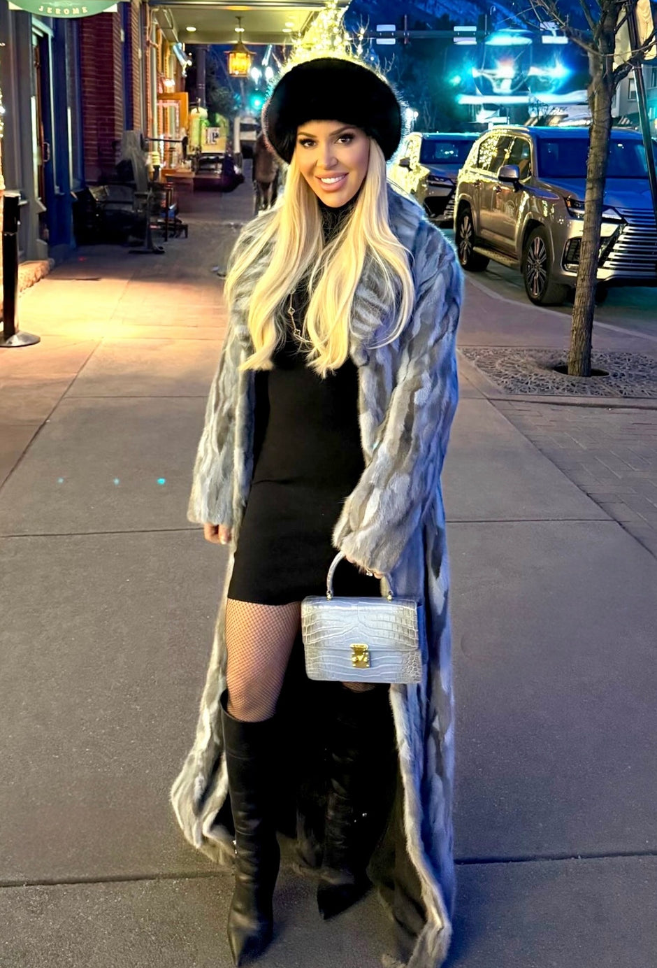 Woman in a long coat and black hat standing on a city street.